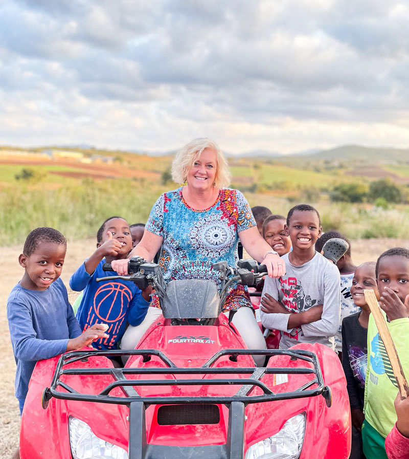 Janine Maxwell on ATV pictured with children in Eswatini, Africa